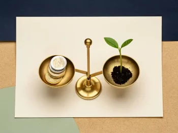 Messing weegschaal met euromunten tegenover een jong plantje op crèmekleurig oppervlak, symbool voor duurzame financiële groei.