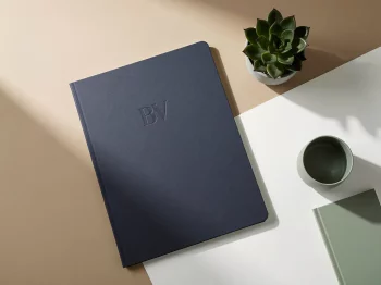 Navy blauwe documentenmap met "BV" reliëf op minimalistische witte bureau met kleine vetplant, natuurlijk licht
