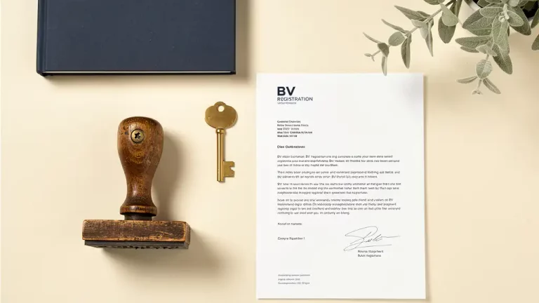 Versleten houten stempel naast BV-registratiedocument op cremekleurig bureau, met messing sleutel als symbool van bedrijfsoverdracht.
