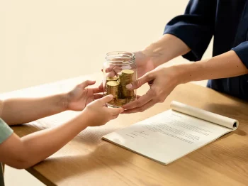 Oudere handen die een glazen pot met gouden munten overdragen aan jongere handen, met een juridisch document op een eiken tafel.