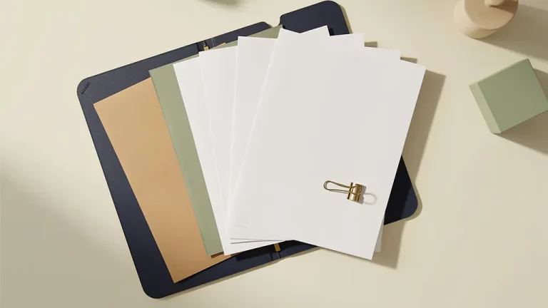 Open documentmap met uitgewaaierde papieren en een messing paperclip op een crèmekleurig bureau, vlak van boven gefotografeerd.