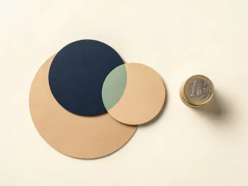 Twee minimalistische cirkels die samensmelten naast een stapel euromunten op een crèmekleurig oppervlak, vlakke bovenaanzicht.