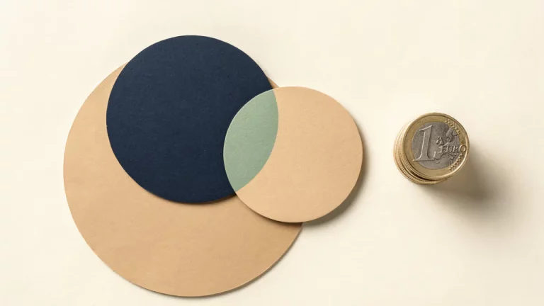 Twee minimalistische cirkels die samensmelten naast een stapel euromunten op een crèmekleurig oppervlak, vlakke bovenaanzicht.