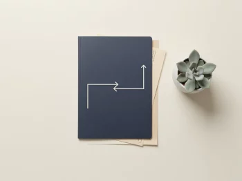 Donkerblauwe documentenmap met pijl die overdracht van ODV-verplichtingen tussen bedrijven symboliseert, naast vetplant op wit bureau
