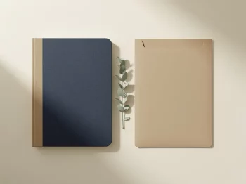 Klassiek pensioendagboek en modern documentenmap naast elkaar op crèmekleurig bureau met groen plantentakje, bovenaanzicht.