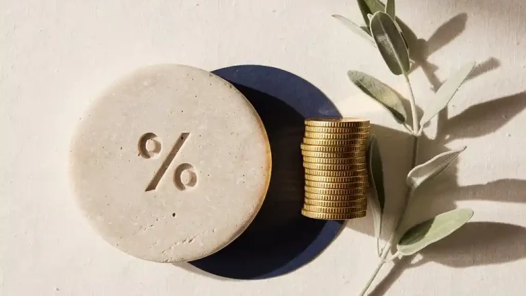 Percentage-symbool gegraveerd in stenen schijf naast stapel gouden munten op crème linnen ondergrond.