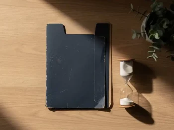 Verweerde documentmap op eikenhouten bureau naast lege zandloper in zacht ochtendlicht, symboliseert vergeten verplichtingen.
